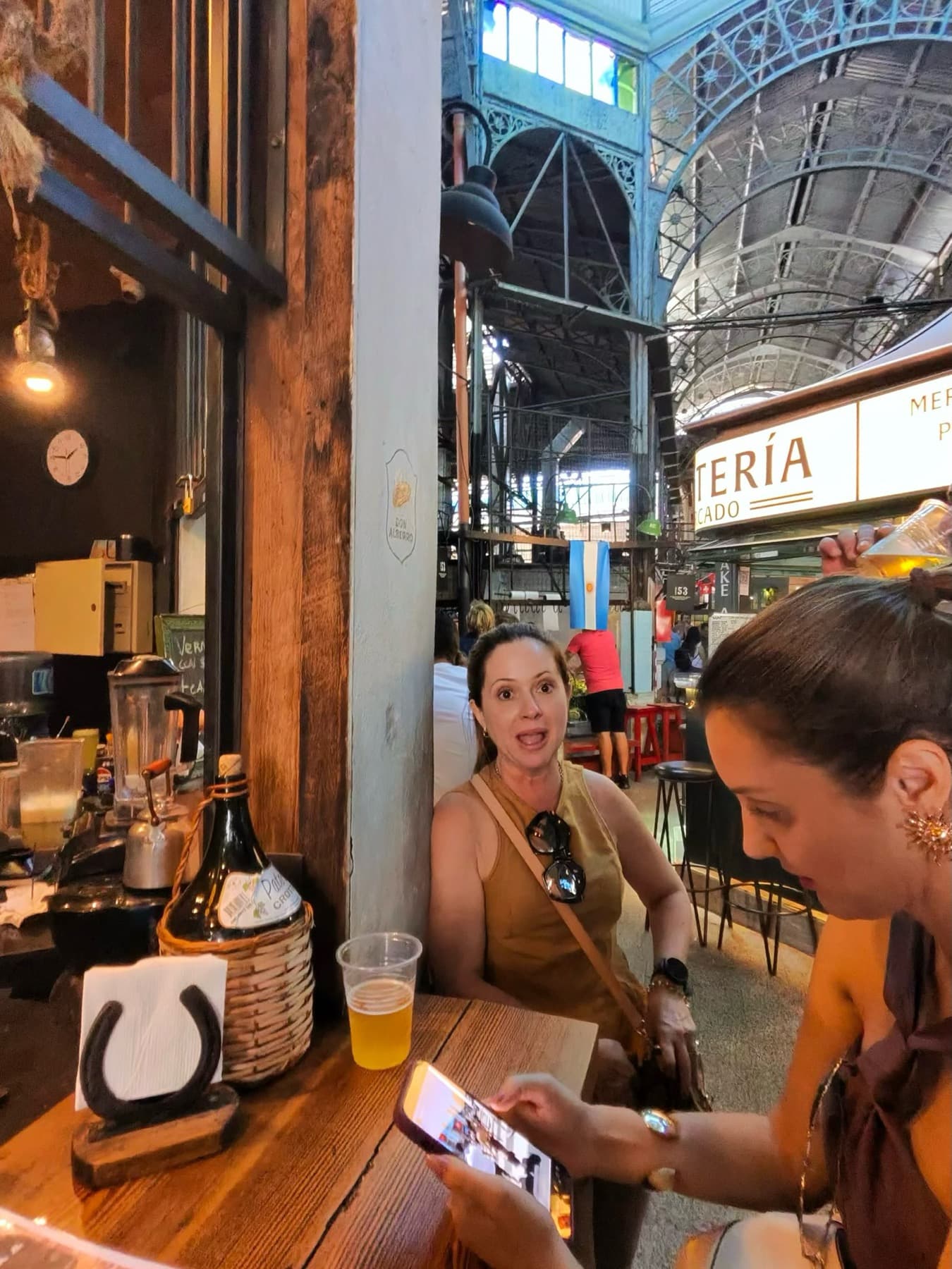Clientes brindando no Mercado de San Telmo, com a estrutura de ferro histórica ao fundo